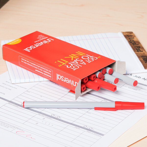 A red box of Universal red medium point oil-based ballpoint stick pens sitting on a piece of paper.