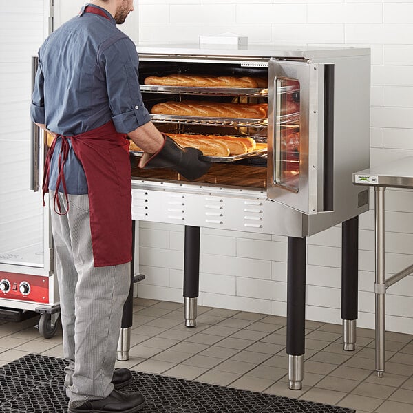 A man wearing an apron standing in front of a Cooking Performance Group convection oven.