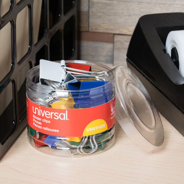 A jar of Universal assorted color binder clips on a table.