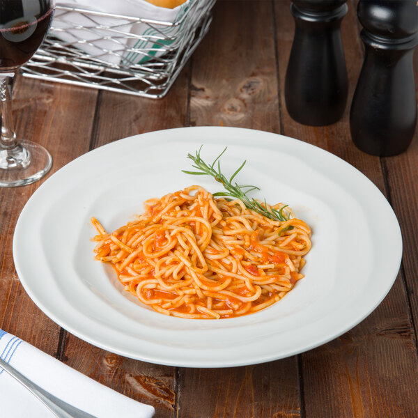 A Tuxton TuxTrendz bright white china pasta bowl filled with spaghetti and a glass of wine on a table.
