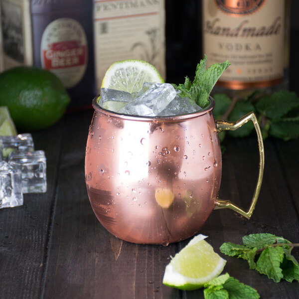 An American Metalcraft copper Moscow Mule mug with ice and mint leaves on a wooden surface.
