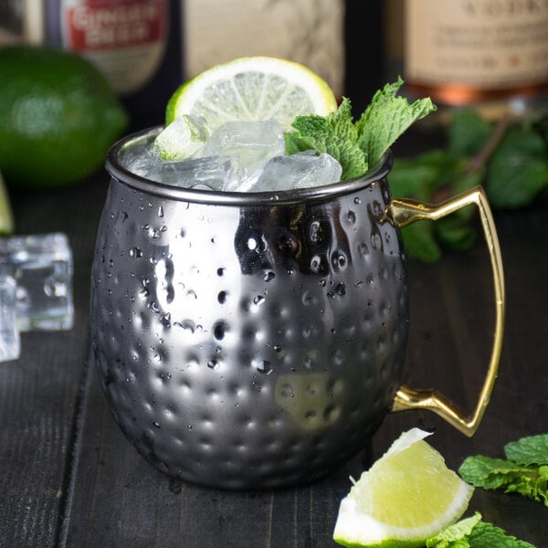 An American Metalcraft hammered black metal Moscow Mule mug with ice and lime slices on top.
