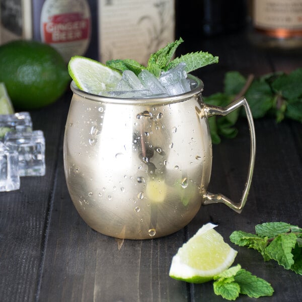 An American Metalcraft mirrored gold Moscow mule mug filled with ice and mint leaves on a wooden surface.