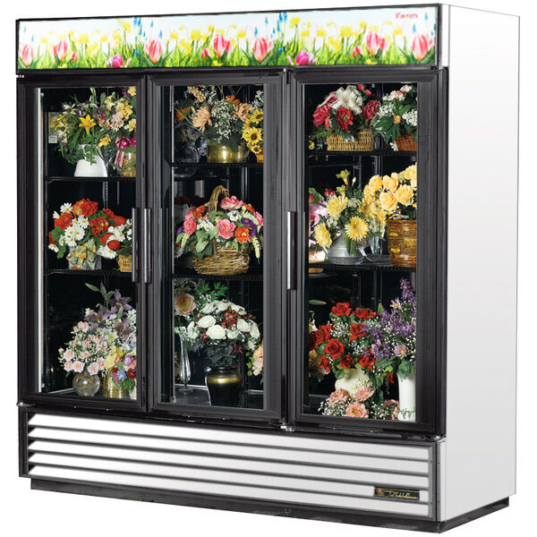 A white True refrigerated glass door floral case with a vase of flowers inside.