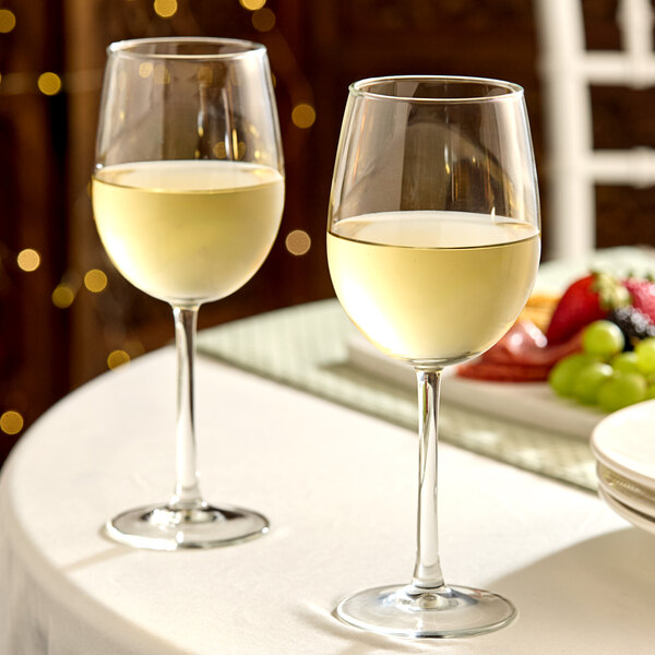 A pair of clear wine glasses filled with white wine on a table.