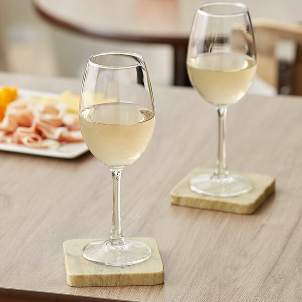 Two Acopa Select Blanc wine glasses of white wine on a table.