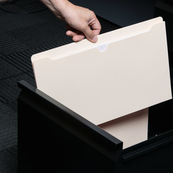 A hand putting a Universal legal size file into a drawer.