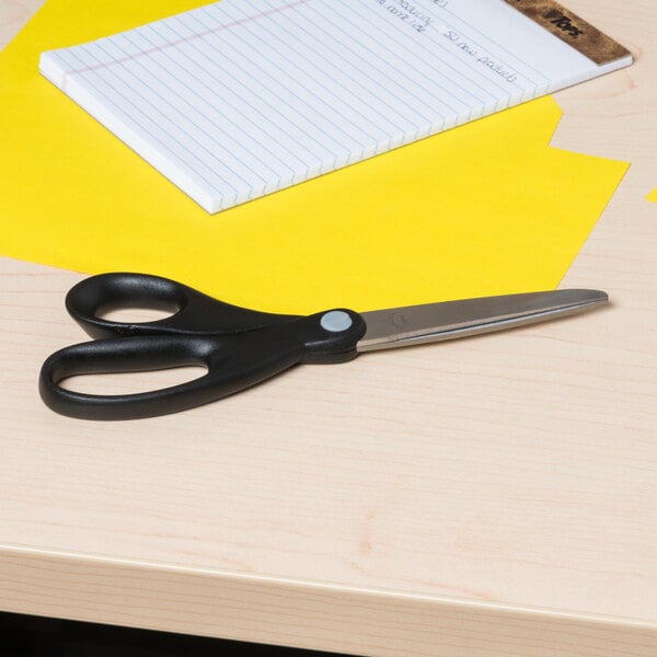 A pair of Universal stainless steel scissors with a black handle on a desk.