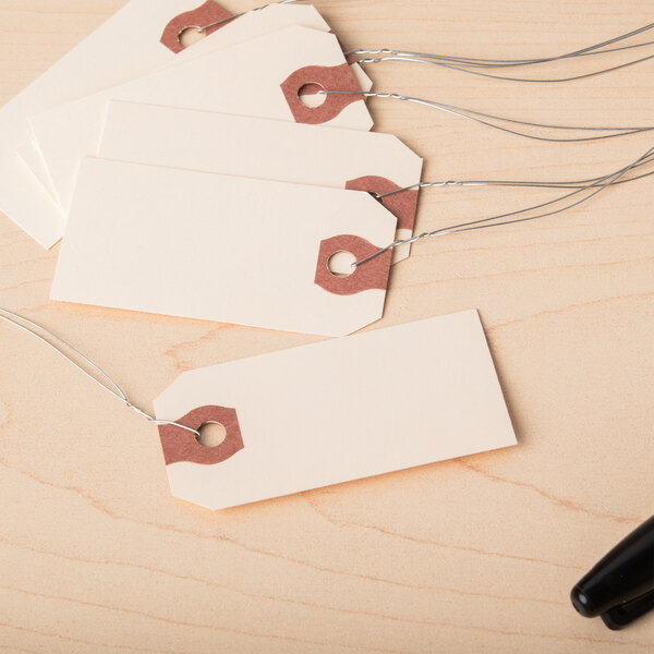 A group of Avery manila wired shipping tags with string and a person holding a black pen.