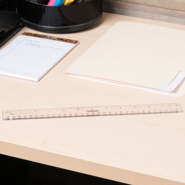 A clear Universal plastic ruler on a desk with a notebook.