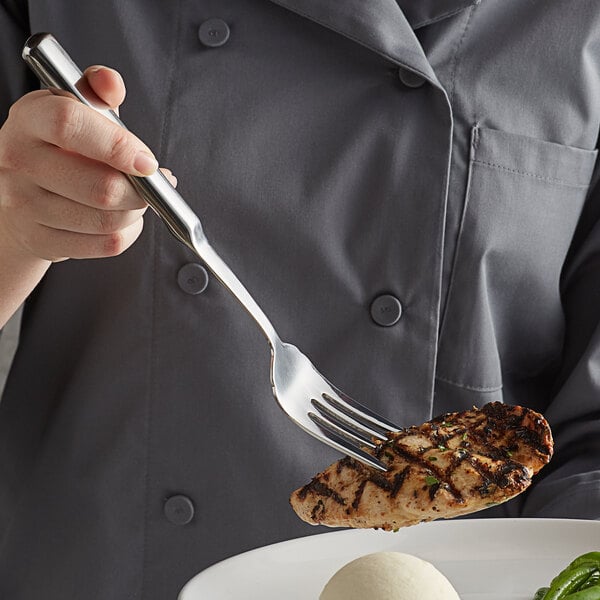 A person holding a Vollrath stainless steel serving fork over a piece of meat.