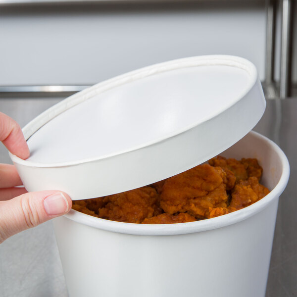 A hand placing a white Double Poly-Paper Soup Cup lid on a container of food.