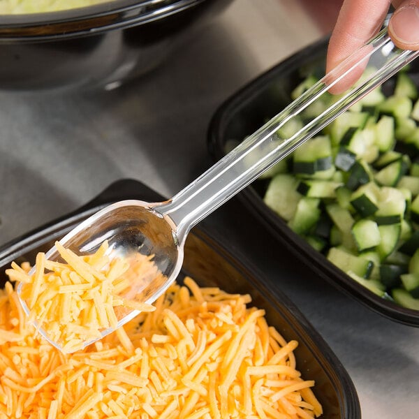 A person using a Thunder Group clear salad bar spoon to scoop shredded cheese into a plastic container.