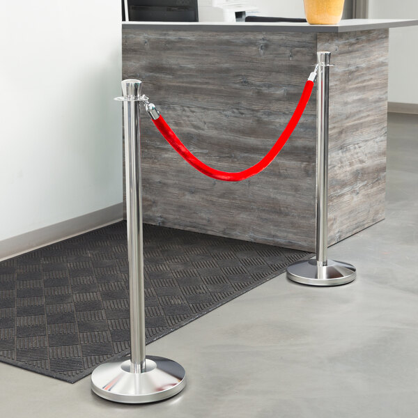 A red rope tied around a Lancaster Table & Seating stainless steel stanchion pole with a crown top.