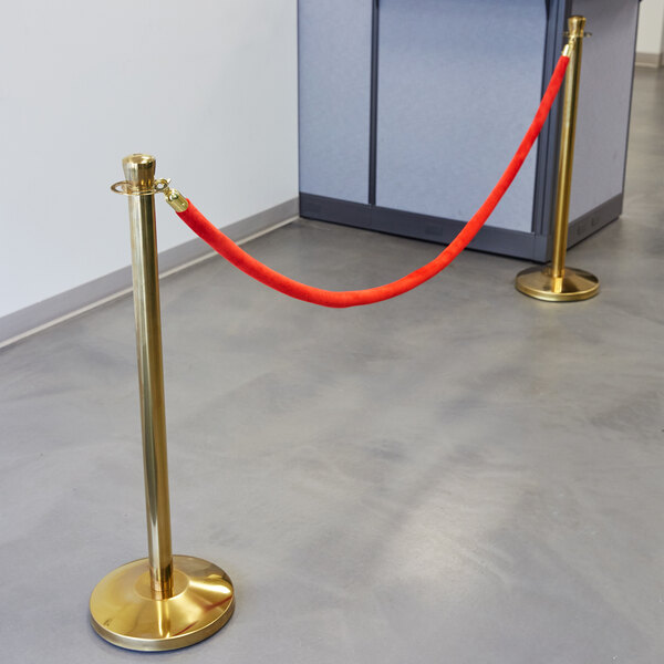 A Lancaster Table & Seating red rope with gold ends attached to a gold stanchion.