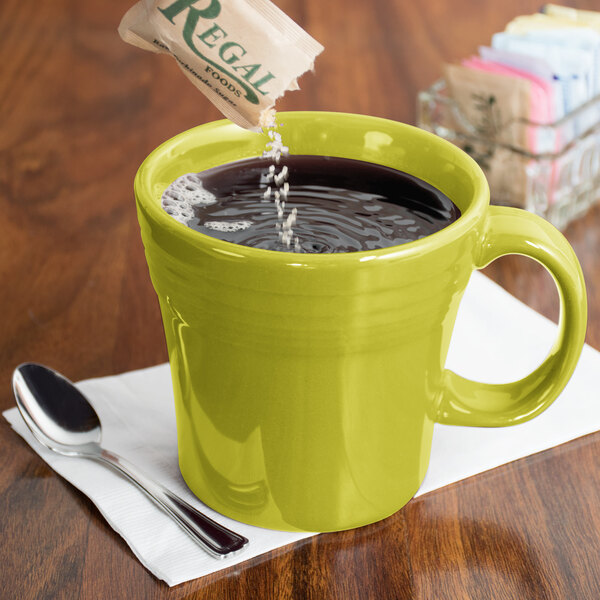 A Fiesta Lemongrass china mug filled with coffee on a counter with a spoon in it.