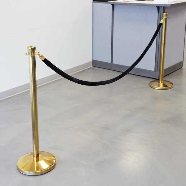 A black stanchion pole with gold ends and a black rope.