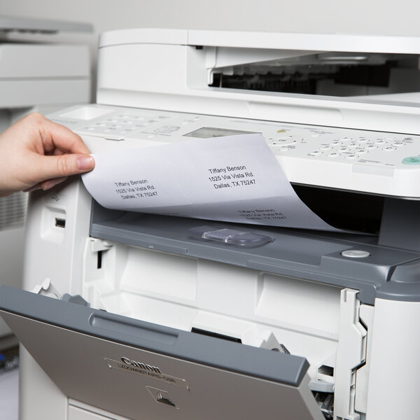 A hand putting a sheet of Avery White Laser Shipping Labels into a printer.