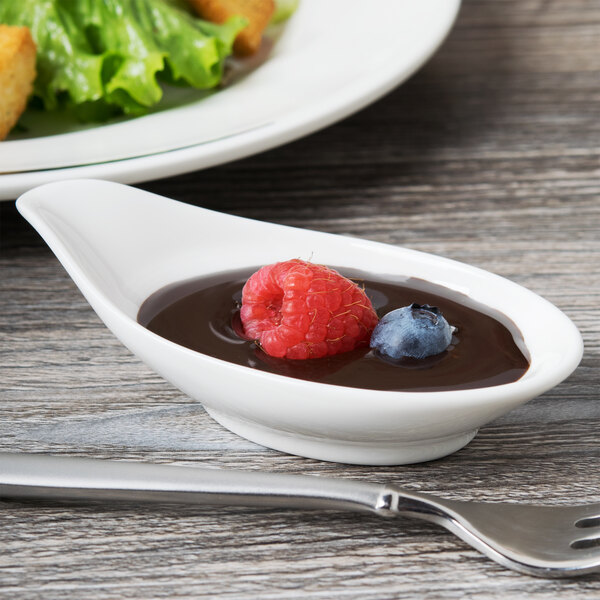 A white porcelain bowl of chocolate sauce with fruit and a fork.