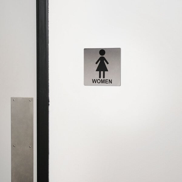 A Tablecraft stainless steel women's restroom sign with a woman symbol on a wall.