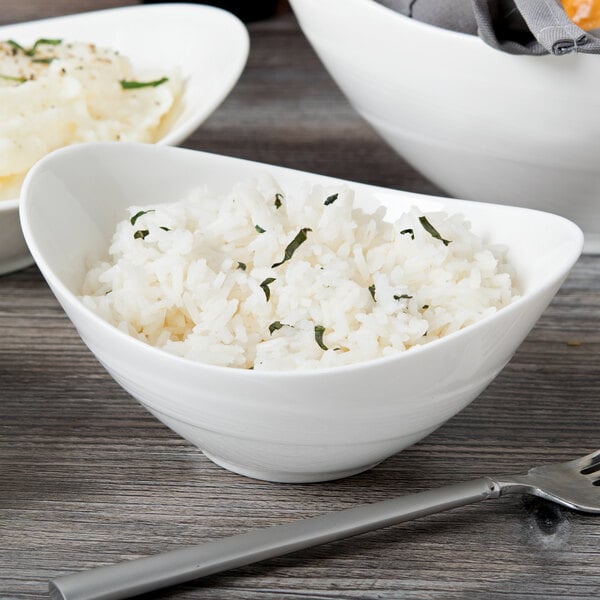 A white oval porcelain bowl filled with rice on a wood table.