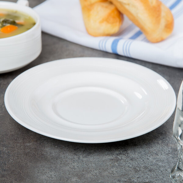 A white porcelain saucer holding a round bowl of soup.