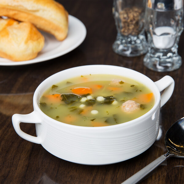 A bowl of soup with vegetables and bread on a table with a spoon and a bowl of soup.
