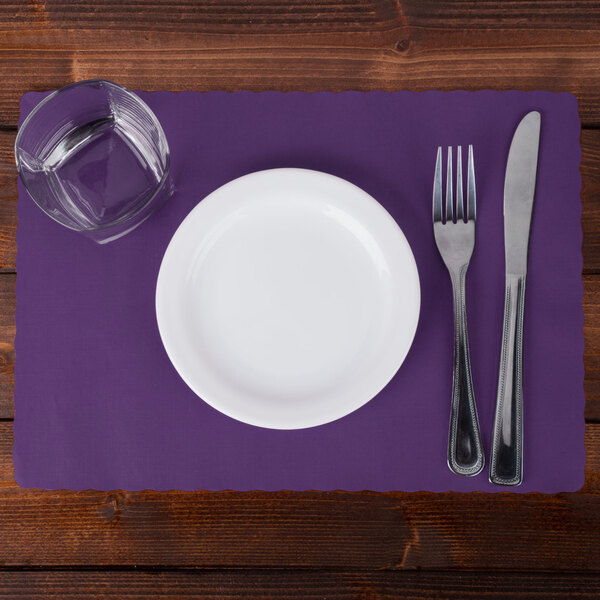 A white plate with a glass of water and a knife and fork on a purple placemat.