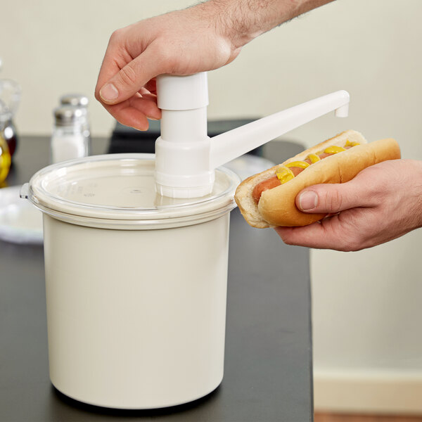 A person's hands using a hot dog to press condiments into a white container with a plastic lid.