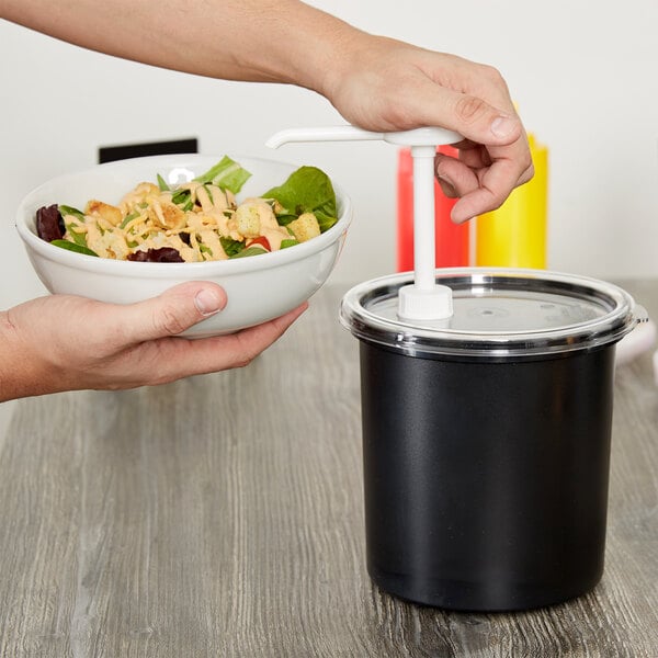 A person holding a bowl of salad next to a black Cambro cold condiment dispenser with a white cap.