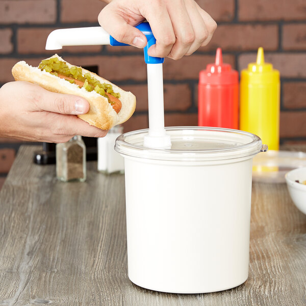 A person holding a hot dog with relish pouring it into a white plastic container with a lid using a black pump.