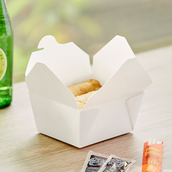 A white Choice microwavable folded paper take-out box filled with food on a table.