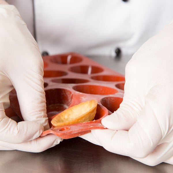 A person in white gloves holding a Matfer Bourgeat orange silicone round tartlet mold filled with food.