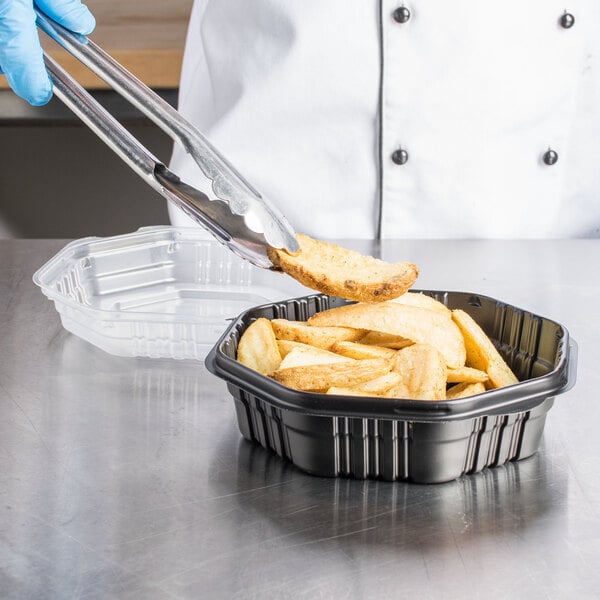A gloved hand holds tongs over Solo black plastic take-out container of food.