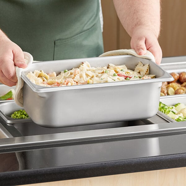 A person holding a Vigor stainless steel steam table pan filled with pasta.