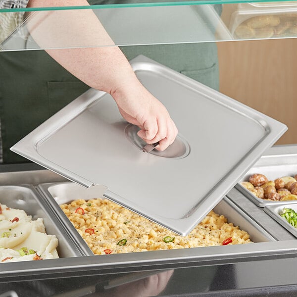 A hand holding a silver tray with a Vigor stainless steel lid open.