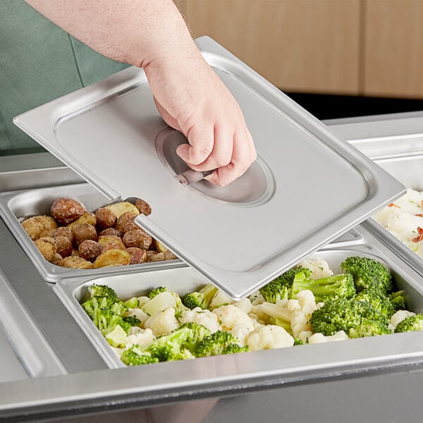 A person holding a Vigor stainless steel steam table pan with food in it.
