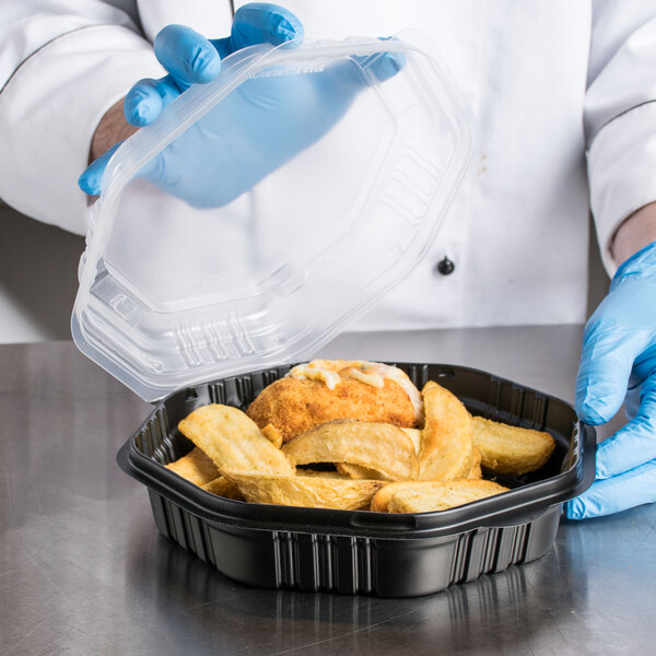 A person in gloves holding a Solo black plastic container of food.