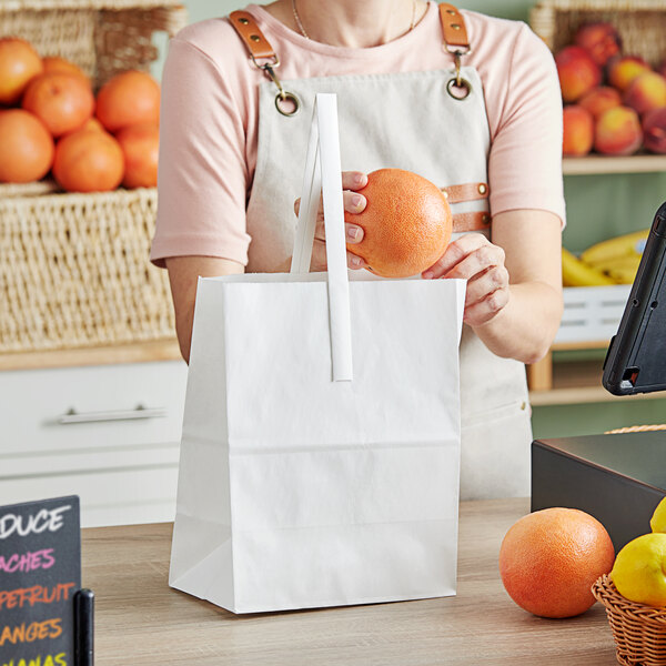 A person holding an orange in a white Choice paper bag.