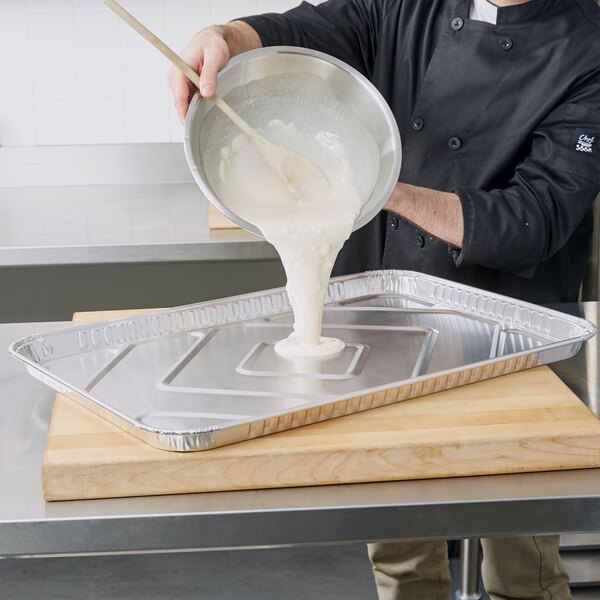 A man pouring white batter from a bowl into a D&W Fine Pack foil cake pan.