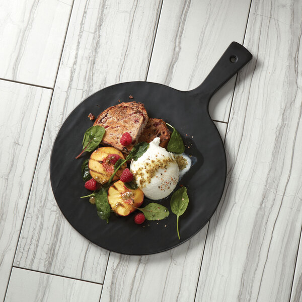 An American Metalcraft black faux slate melamine serving peel with a plate of food on a marbled surface with a slice of fruit and a spoon.