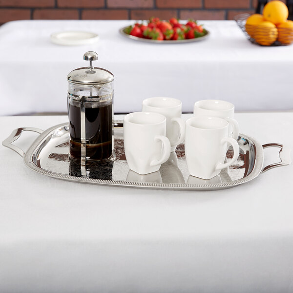 A Vollrath stainless steel oblong serving tray with coffee and white mugs on it.