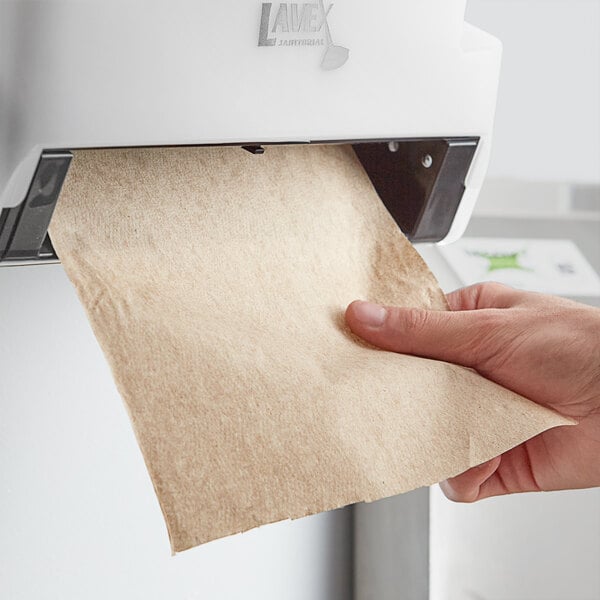 A hand holding a piece of paper in front of a Lavex hardwound paper towel dispenser.