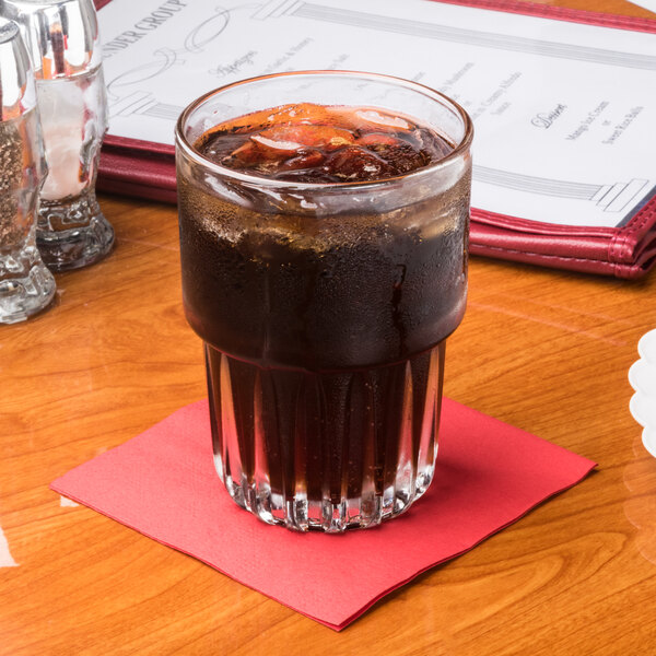 A glass of soda with ice on a table with a red Hoffmaster cocktail napkin.