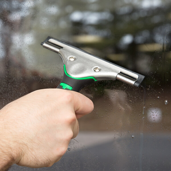 A hand holding a Unger ErgoTec window squeegee cleaning a window.