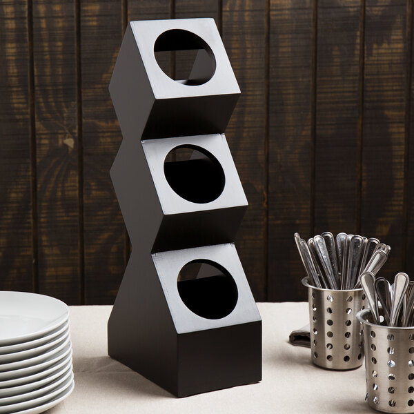 A black metal Cal-Mil vertical stand with three silver containers with holes.