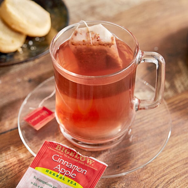 A glass mug of Bigelow Cinnamon Apple Herbal Tea with a tea bag in it.