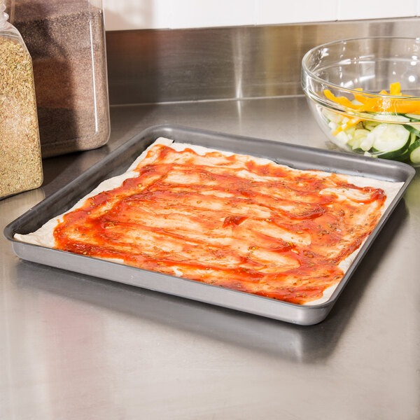 An American Metalcraft square pizza pan with a pizza on it on a counter.
