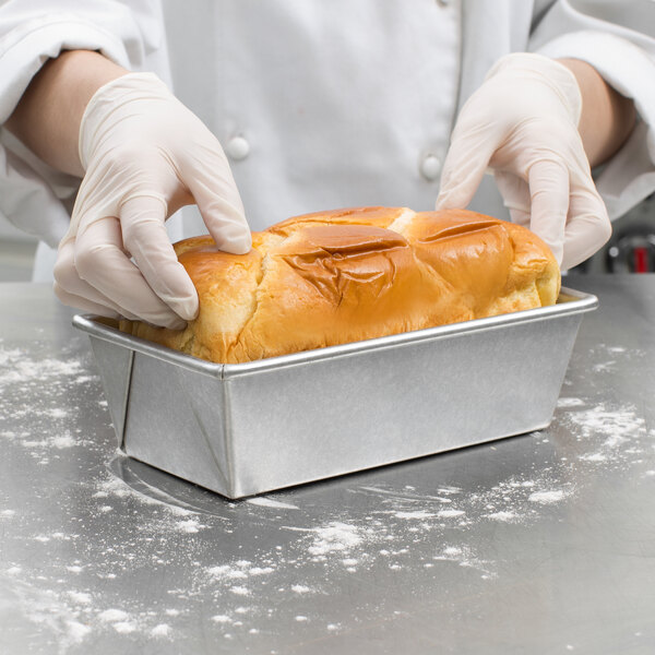 A person in white gloves holding a loaf of bread in a Chicago Metallic aluminized steel bread loaf pan.