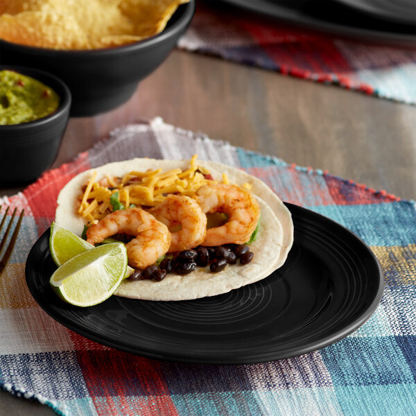 A Tuxton Concentrix black china plate with shrimp tacos, guacamole, cheese, and beans.